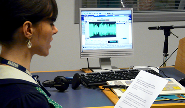 Woman reading a script aloud sitting in front of a computer moniter